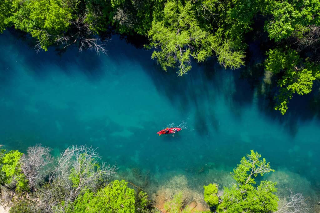 Aerial view of a person kayaking in a narrow, clear blue river surrounded by dense green trees, reminiscent of the serene escapes nonprofit lawyers dream about in their quest to guide nonprofit organizations.