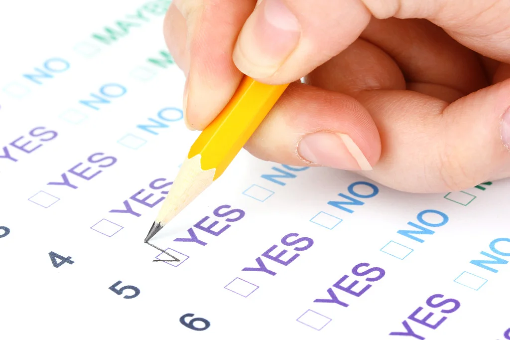 A hand holds a yellow pencil, marking the "YES" box on a nonprofit compliance checklist form.
