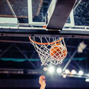 A basketball is seen going through a hoop with a player's hand extended upward underneath the net, showcasing the skill nurtured by a professional athlete's foundation.