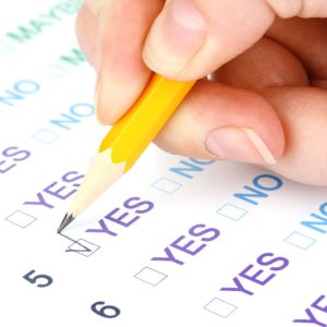 A hand holds a yellow pencil, marking the "YES" box on a nonprofit compliance checklist form.