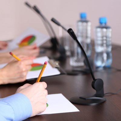 People's hands are shown writing on paper, with pie charts visible, at a conference table discussing complaints against a nonprofit.