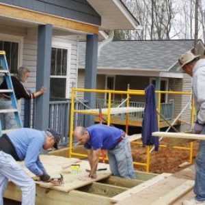A group of people work on a wooden ramp outside a house, embodying the community-driven spirit often seen in the duties of nonprofit board of directors.